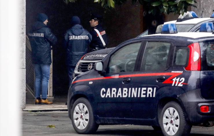 Macchina dei carabinieri in primo piano, forze dell'ordine davanti ad un palazzo